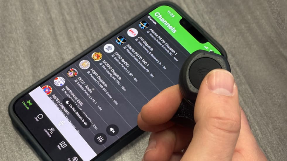 Closeup photo of man's hand using a thumg to push a push to talk button with phone on table.