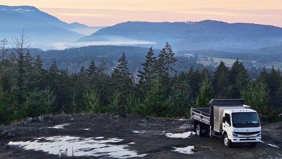 Electric truck parked in front of a scenic mountain background.