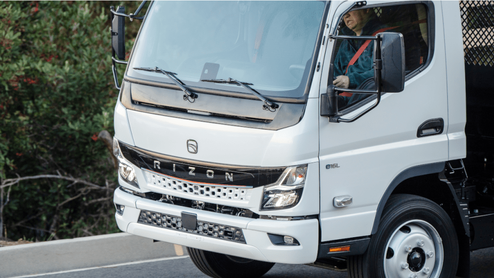 close-up photo of a man driving a white battery electric truck.