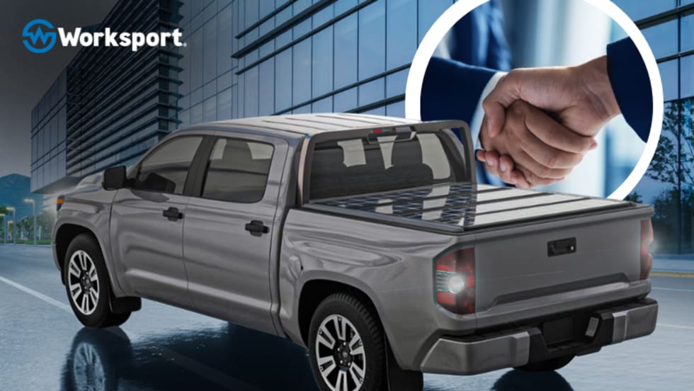 Truck with a tonneau cover on the bed, company logo for Worksport, and inset photo of two men shaking hands.