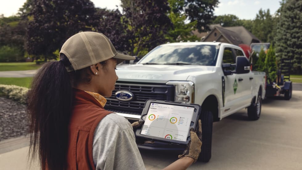 Woman worker looking at telematics on a tablet with a Ford work truck in the background. 