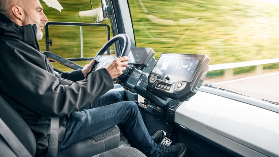 Man inside the cab of a futuristic looking truck driving.