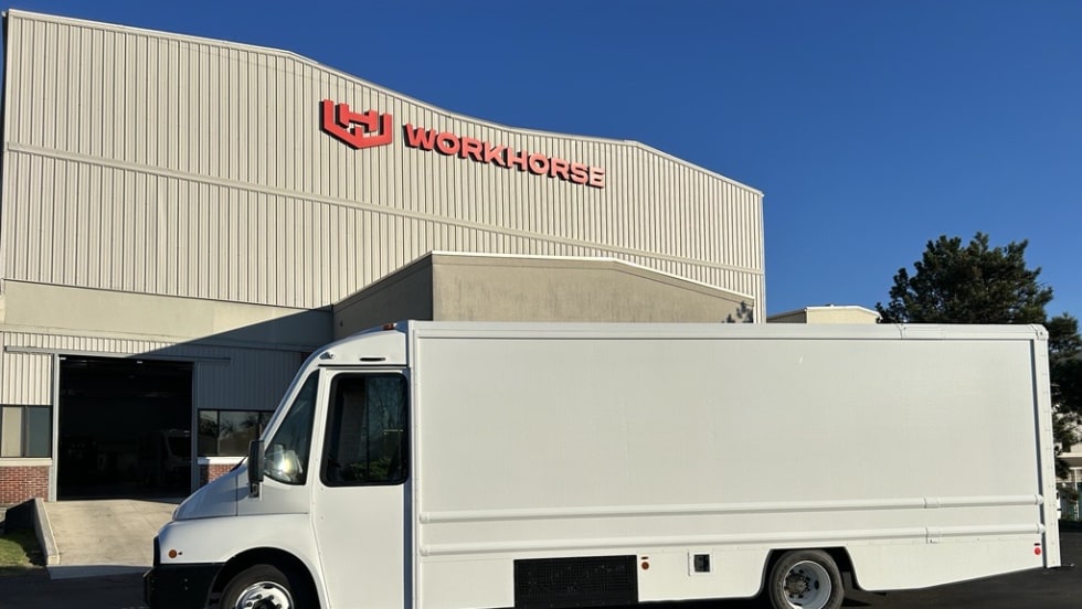 Side view of an electric step van parked in front of a building with a Workhorse sign.