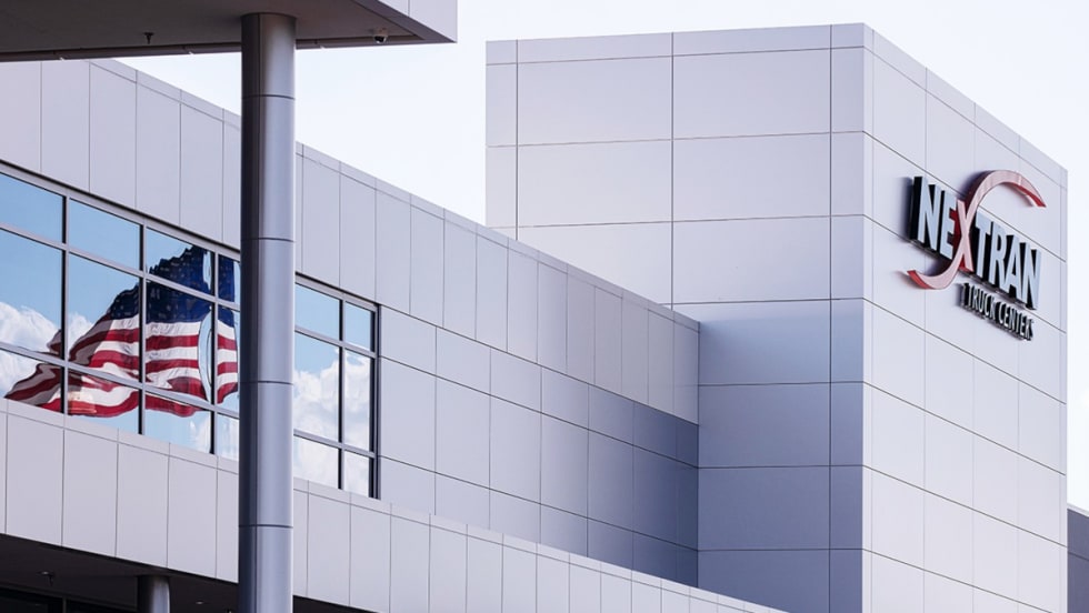 Office building marked by a sign that says Nextran, American flag reflected in a window.