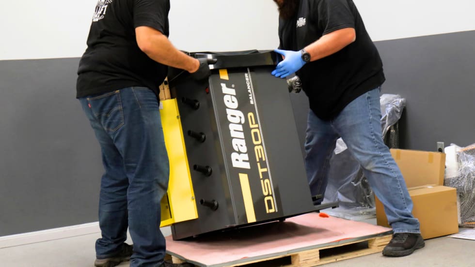 Men lifting a piece of industrial equipment off a wooden pallet.