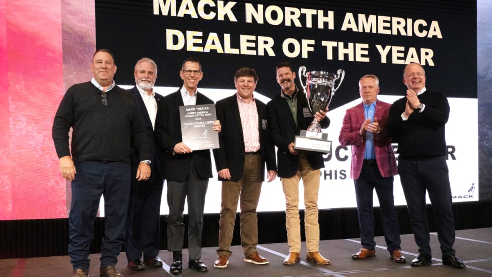Group of businessmen on a stage presenting and receiving an award trophy.