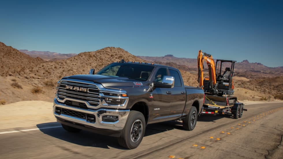 Ram HD pickup towing a mini excavator on a trailer in the desert.