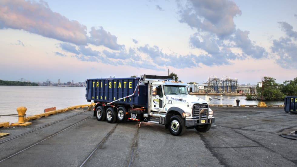 Mack Granite with roll-off container parked in a port area.