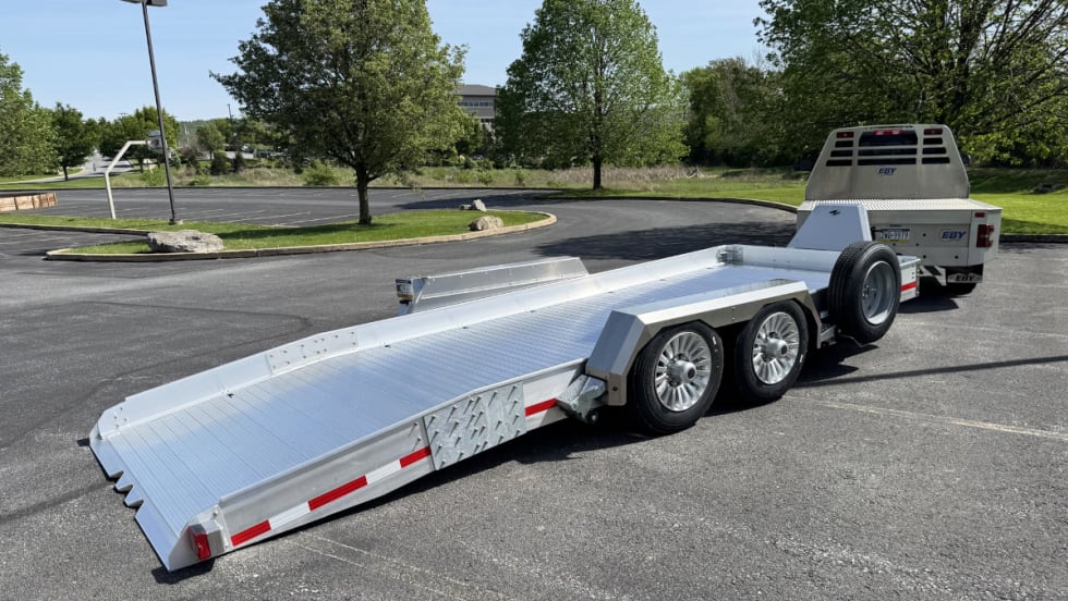 Rear quarter view of an aluminum kneeling trailer hitched to a truck.