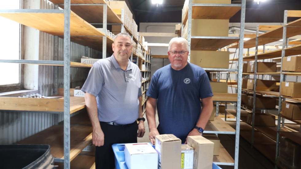 Two men standing in a parts warehouse with shelving and boxes.