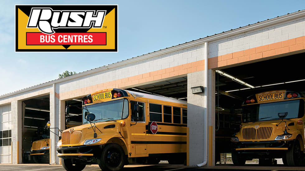 Two yellow school buses are parked in service bays at a dealership under the Rush Bus Centres logo.