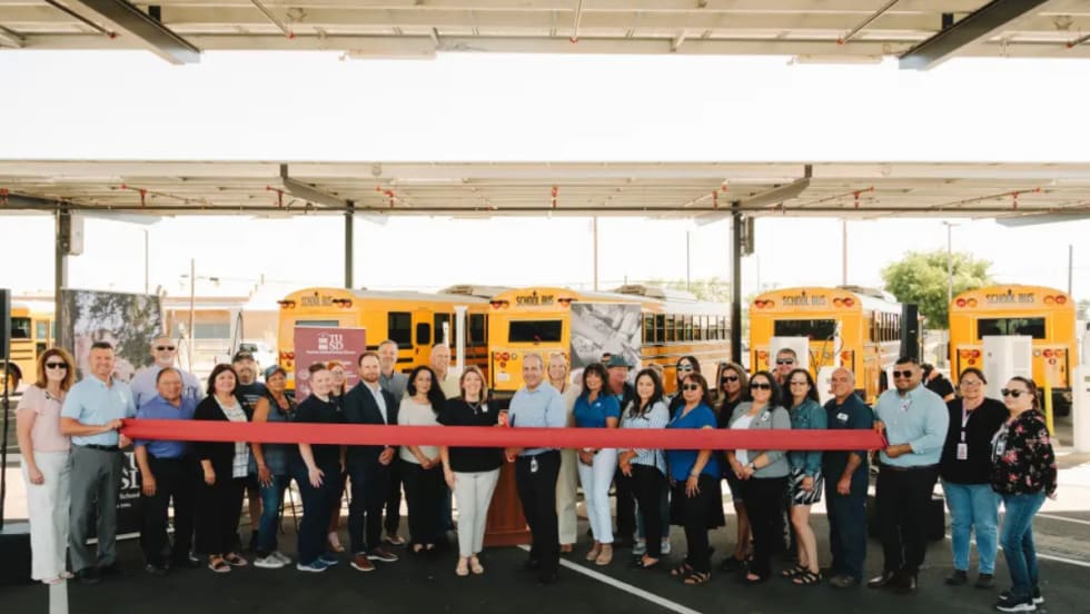 Turlock Unified staff and partners hold a ribbon-cutting in front of new electric school buses under solar canopies at the district transportation center.