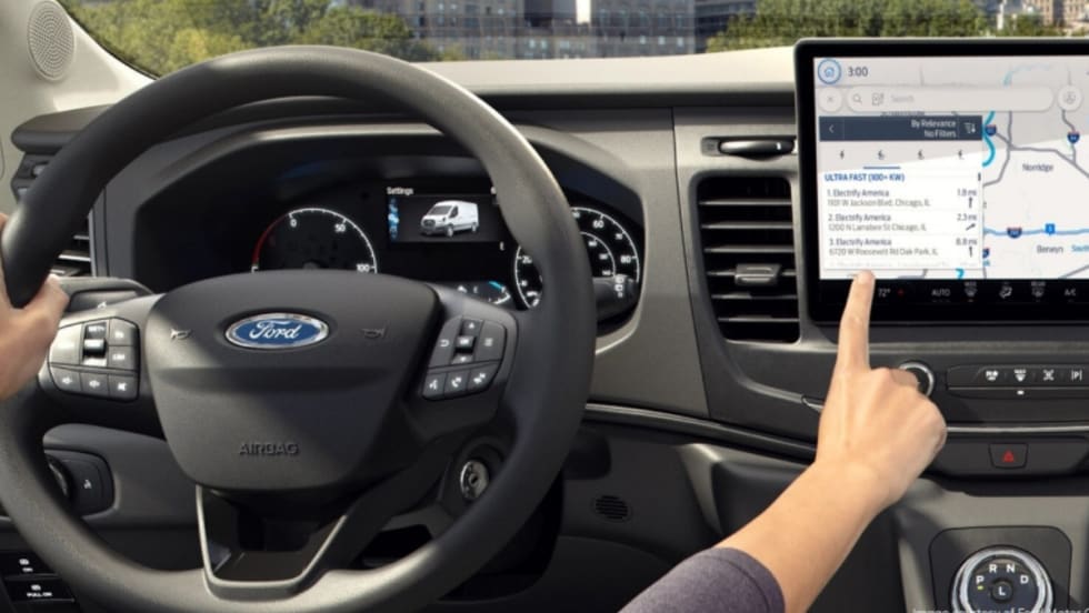 Driver inside a Ford electric vehicle uses the touchscreen navigation system to locate nearby ultra-fast charging stations, illustrating EV operational tools for fleet drivers.