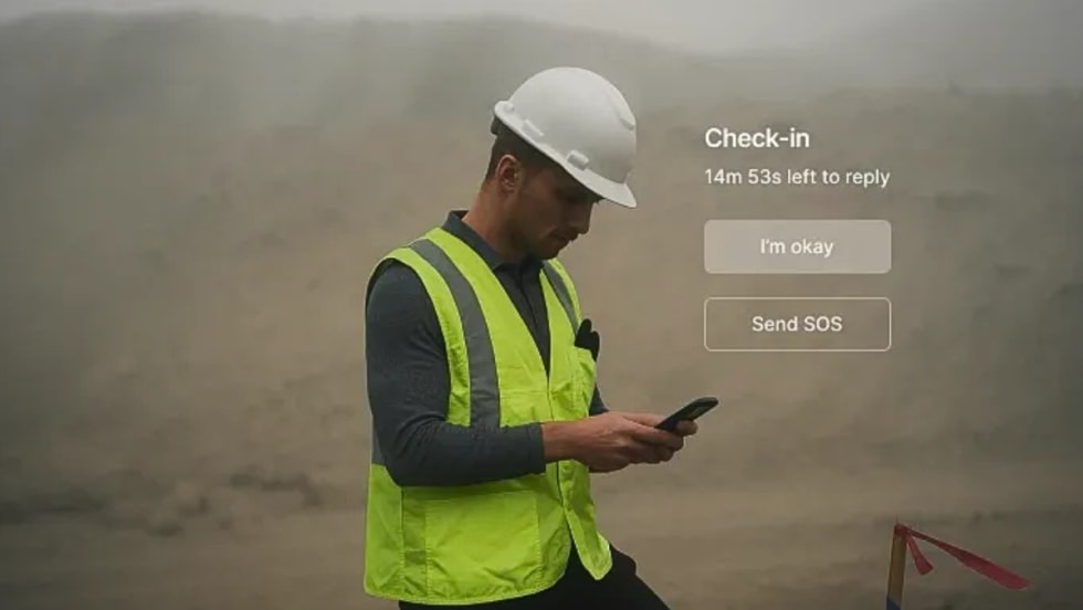 Worker in hard hat and safety vest checks phone with “I’m okay” and “Send SOS” safety check-in options on screen.
