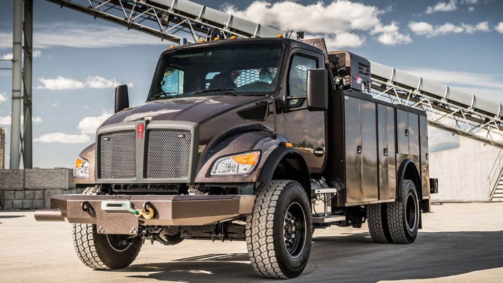 A Kenworth T480 vocational truck with off-road tires and utility service body parked outdoors under a blue sky, showcasing its rugged design for demanding worksite applications.