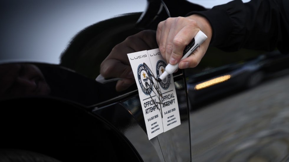A close-up of a person sealing two Guinness World Records “Official Attempt” stickers on the side of a Lucid vehicle with a marker, reflecting the vehicle's record-setting range attempt.