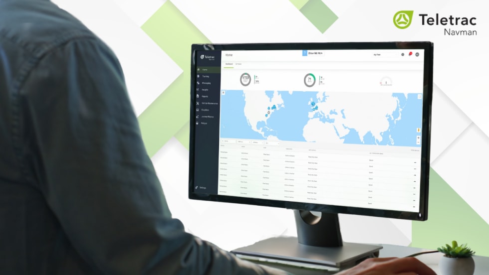 Person using Teletrac Navman’s TN360 fleet management platform on a desktop monitor displaying a world map and vehicle data, with the Teletrac Navman logo on a light background.