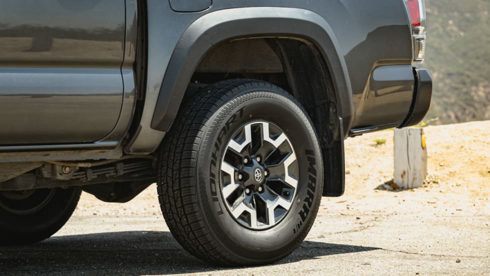 Closeup photo of the rear left tire of a pickup truck parked in a dirt area.