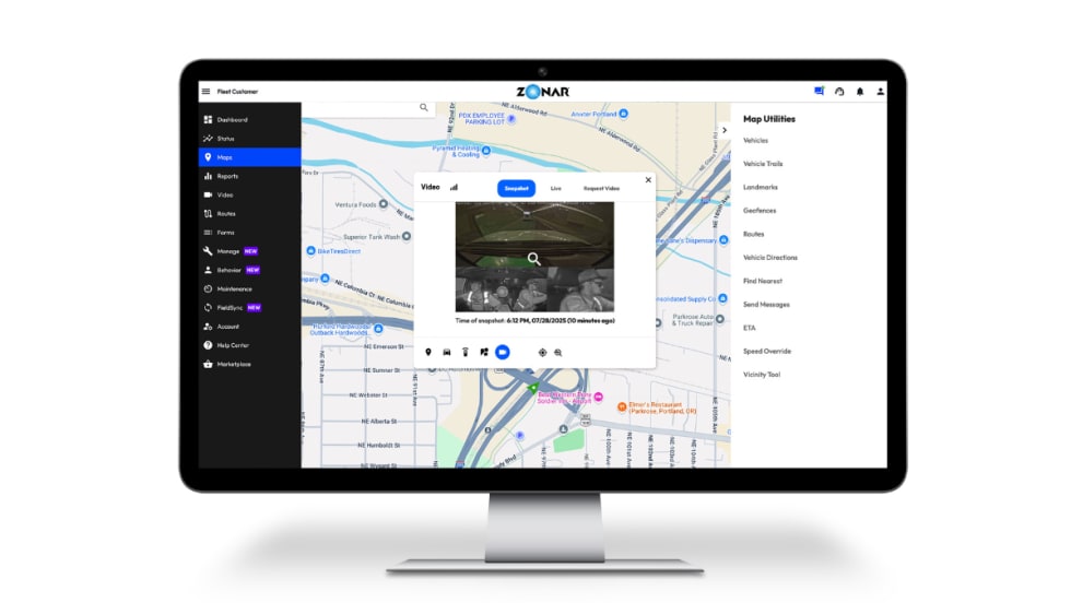 Computer monitor displaying Zonar Ignition’s fleet management interface, showing a city map with vehicle locations and an inset video snapshot from inside a vehicle’s cabin.