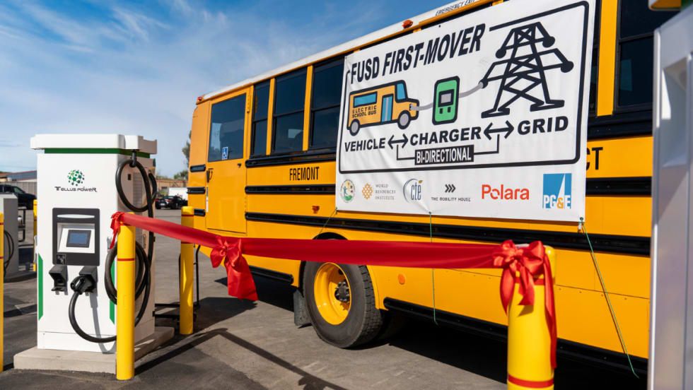 Fremont USD electric school bus next to a Tellus Power bidirectional charger with ribbon, marking launch of V2G system to support grid resilience and clean energy initiatives.