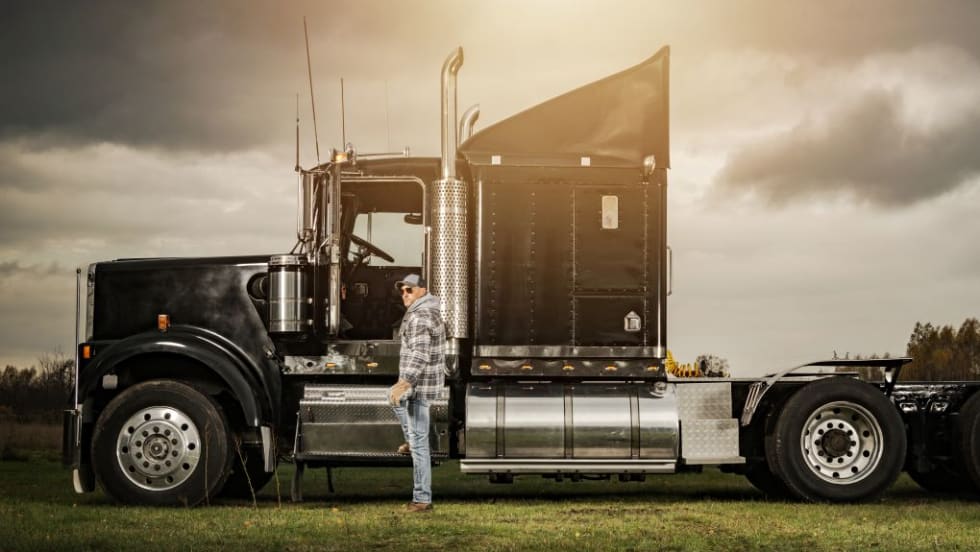 Moody photo of a black classic style commercial truck with a driver standing beside it.