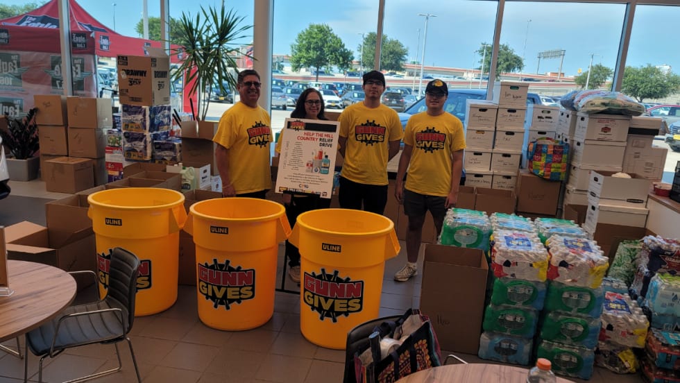 Gunn Auto Group volunteers stand with collection bins and donated supplies for the Help the Hill Country relief drive after devastating floods in Central Texas.