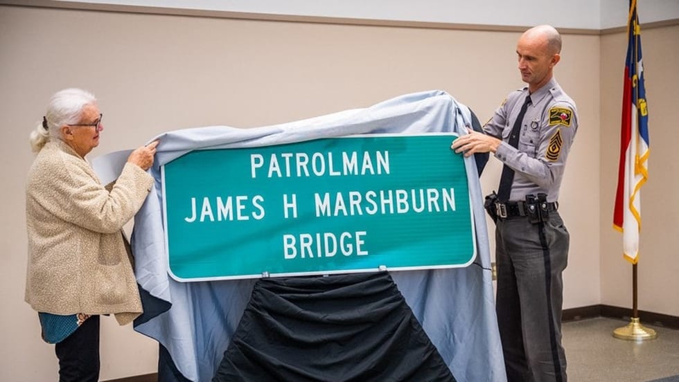 Police officer and elderly woman unveiling Patrolman James H Marshburn Bridge sign