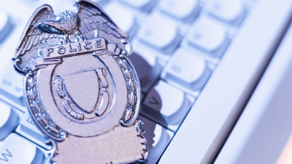 Silver police badge with eagle emblem resting on computer keyboard