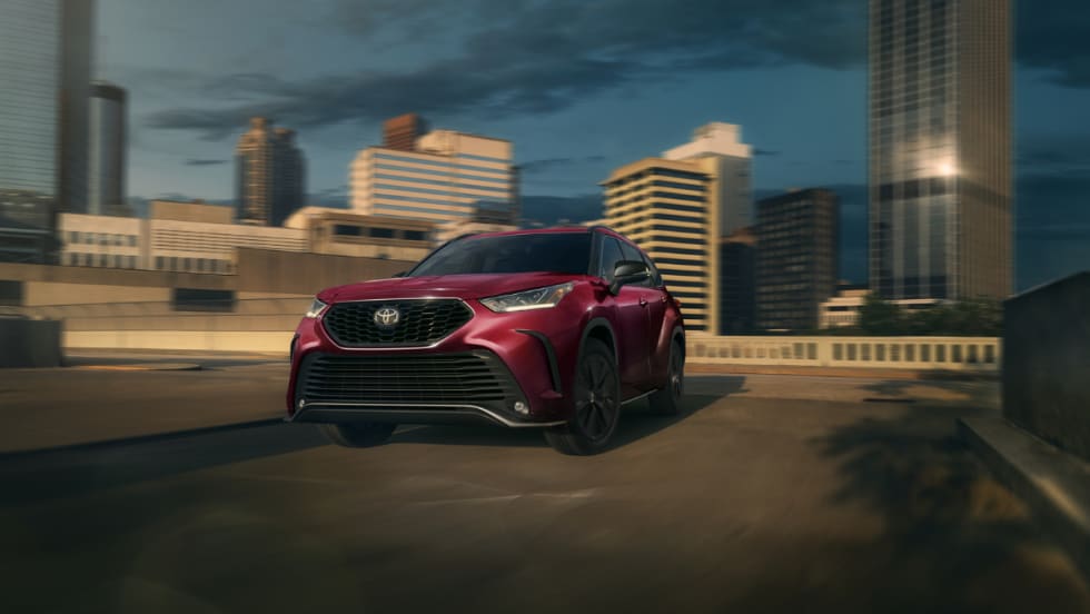 Red Toyota SUV driving through urban cityscape at sunset.