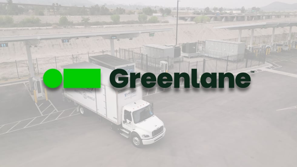 Greenlane logo overlaid on a picture of a Velocity electric truck parked at Greenlane’s Colton, California charging site with multiple charging stations visible.