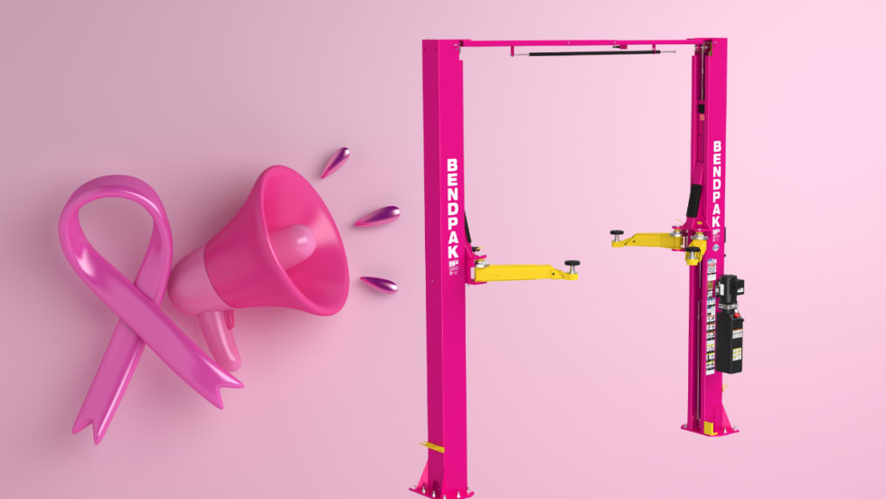 Pink BendPak two-post car lift with yellow arms, shown alongside a pink ribbon and megaphone symbolizing breast cancer awareness.