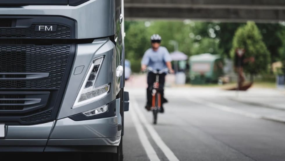 Close-up of a Volvo FM truck front with a cyclist approaching on the road, illustrating Euro NCAP’s focus on truck safety and protection for vulnerable road users.