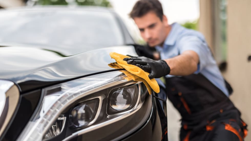 Technician polishing a car headlight with a microfiber cloth, representing Protective Asset Protection’s enhanced Appearance Protection program for long-term vehicle surface care.