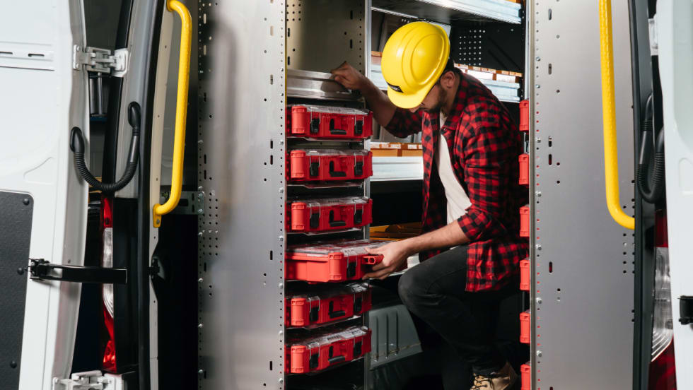 A worker in a van installing red Milwaukee Packout toolboxes into a Ranger Design Partskeeper Cabinet system.