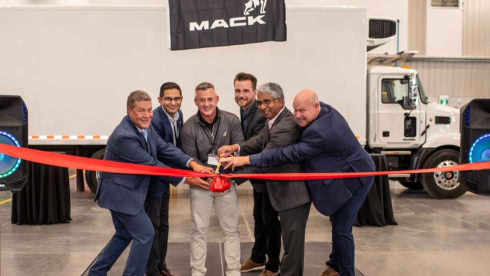 Mack Trucks and TransWestern Truck Centres representatives cut a red ribbon at the opening of the new Calgary dealership with a Mack truck in the background.