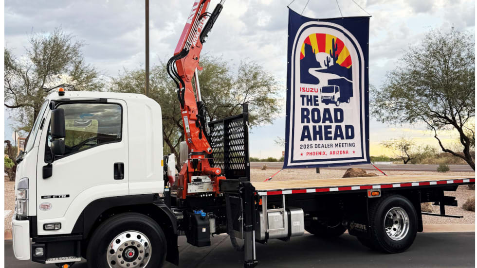 Flatbed Isuzu truck with a sign on back promoting The Road Ahead, the company's annual dealer meeting.