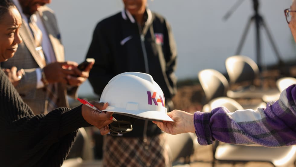 Close-up of a construction hard hat being handed to an attendee at the Normandy Schools Collaborative groundbreaking event.
