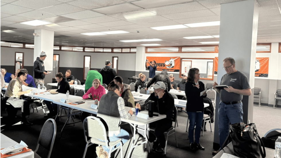 Group[ of people working and talking in a classroom setting.