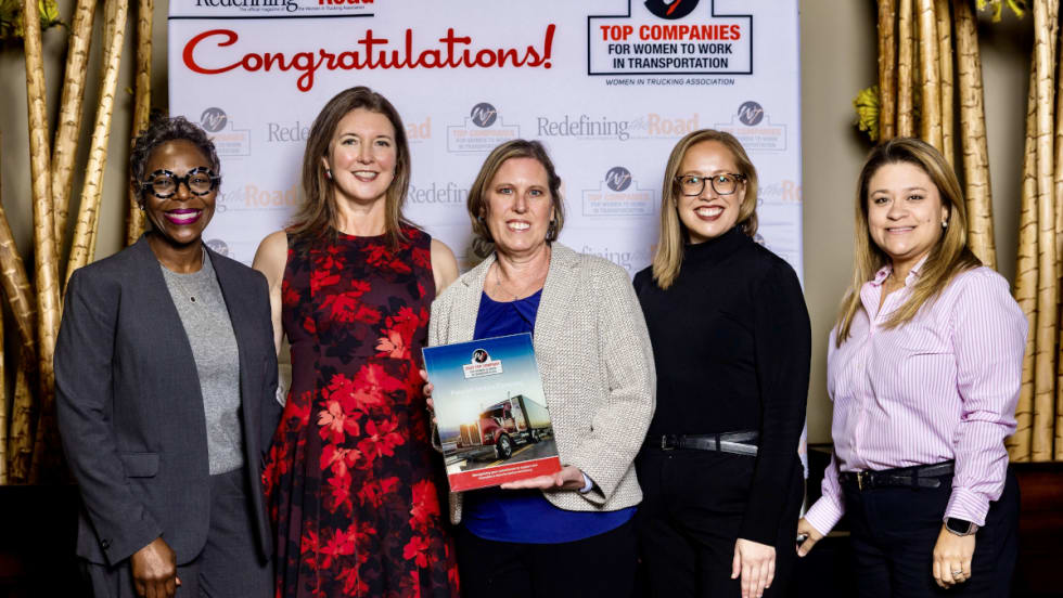 Five women stand on stage together after receiving an award.