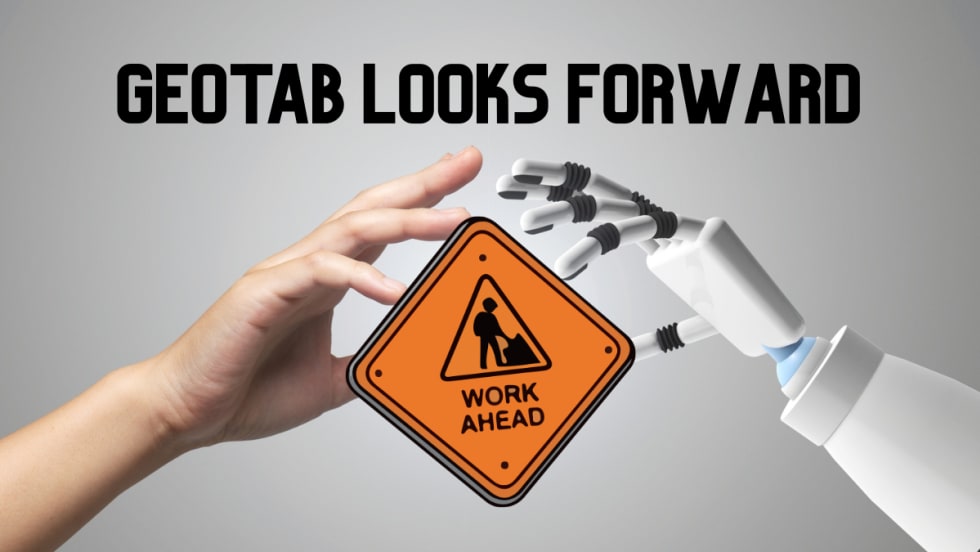Human and robot hands hold a road sign reading Work Ahead, representing Geotab’s 2026 fleet predictions focused on AI, autonomy, and data quality.