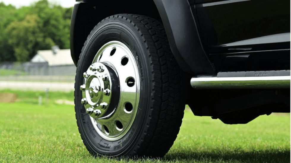 Closeup photo of a front left truck tire on a black truck parked on grass.