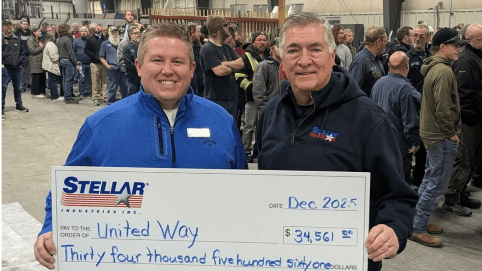Photo or one man presenting a large check to another man with people in the background.