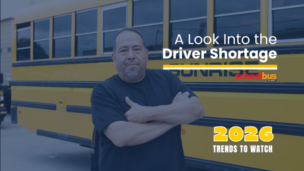 School bus driver stands with arms crossed in front of a yellow Sunrise school bus, with text reading “A Look Into the Driver Shortage” and “2026 Trends to Watch” from School Bus Fleet.