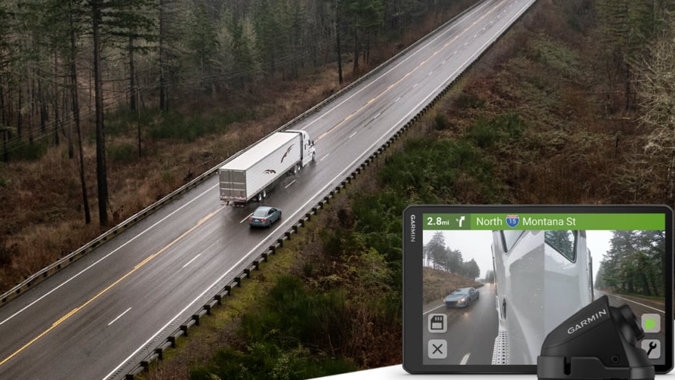 An overhead view of a tractor-trailer traveling on a two-lane highway, with an inset showing a Garmin in-cab display and side-mounted camera view of a passing vehicle.