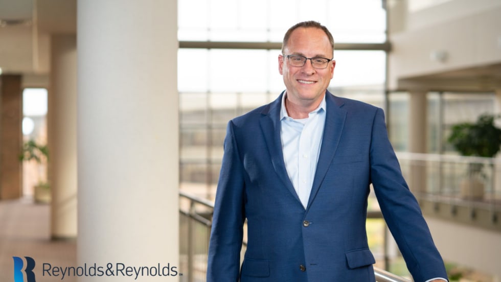 Chris Walsh, president and acting CEO of Reynolds and Reynolds, standing inside an office building wearing a blue suit.