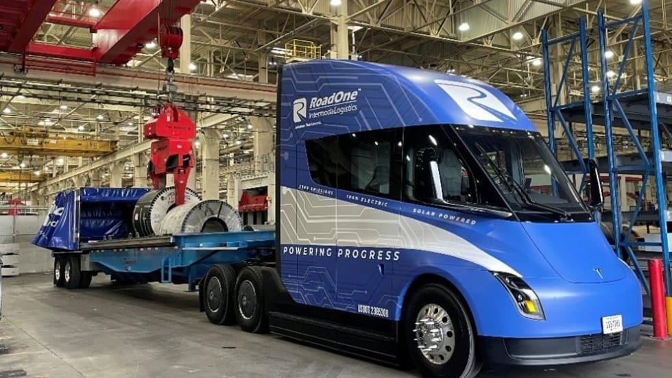 Blue Tesla Semi pulling flatbed trailer inside warehouse or manufacturing facility