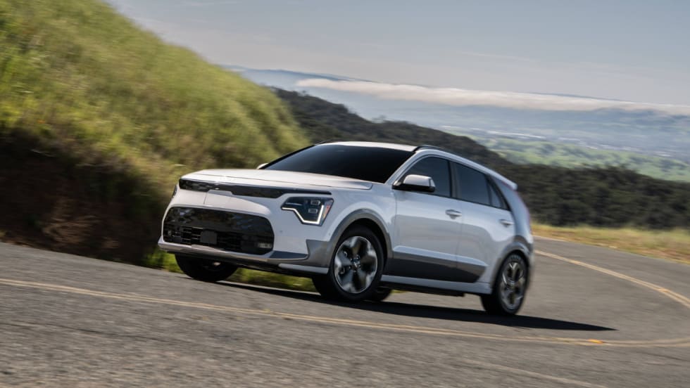 2026 Kia Niro EV driving on a winding road through a hilly landscape.