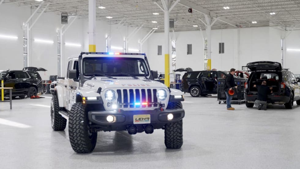 Police Jeep with light activated inside a garage with other vehicles being worked on in the background.