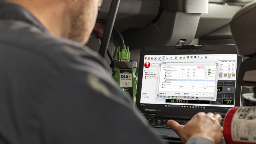 Technician using diagnostic software on a laptop connected to a commercial vehicle to analyze CAN bus data.