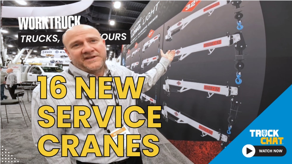 Man standing and talking in front of a trade show wall showing different models of cranes with logos for Work Truck and Truck Chat and headline 16 New Service Cranes.